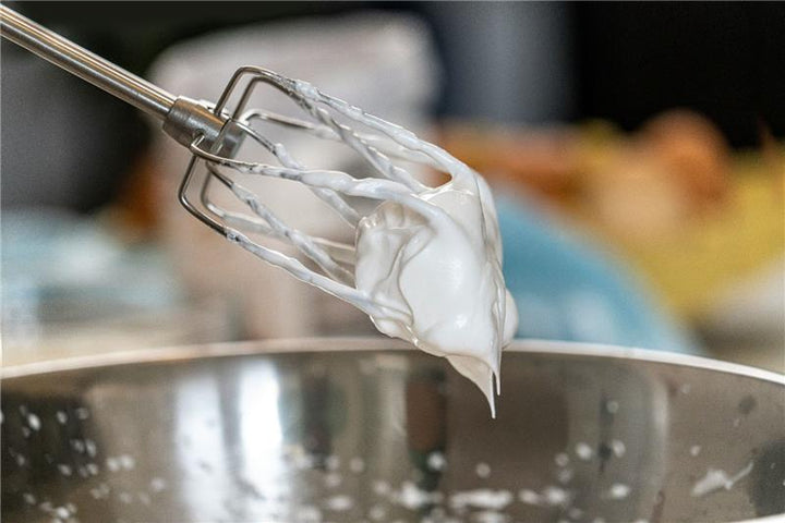 Handmixer covered in whipped cream over a metal bowl